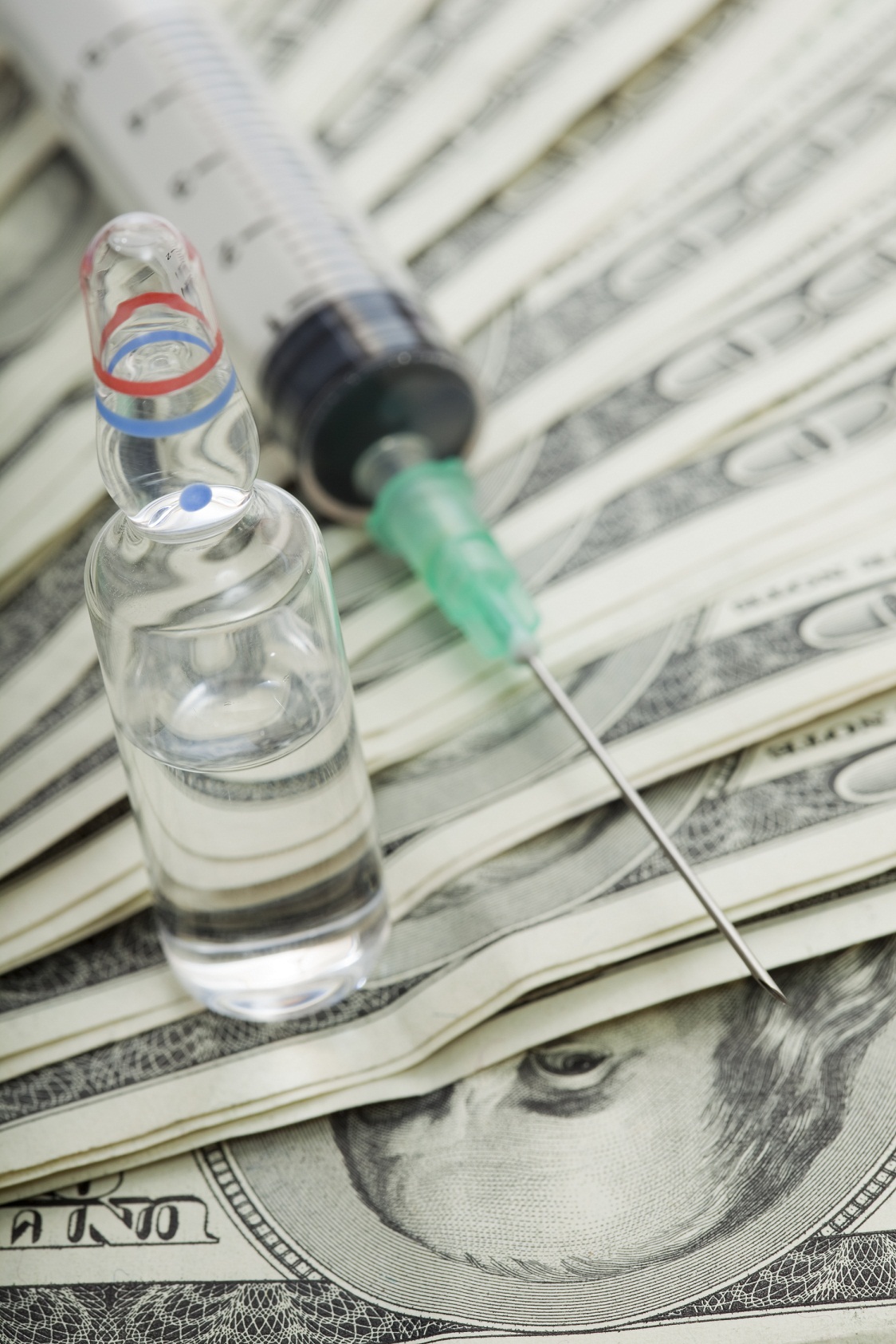 Syringe and ampoule with medicine on banknotes one hundred dollars.
